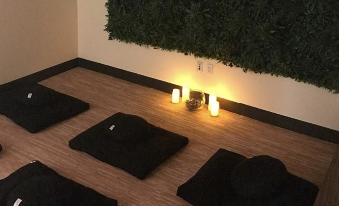 Candles are lit in a dim room with meditation mats spread equally among the floor.